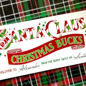 May include: A white card with red and green text that reads "SANTA CLAUS CHRISTMAS BUCKS". The card has a red and green striped design and stars. The text "DELIVER TO: Alexander FROM THE MONEY VAULT OF: Santa Claus" is printed on the bottom of the card.