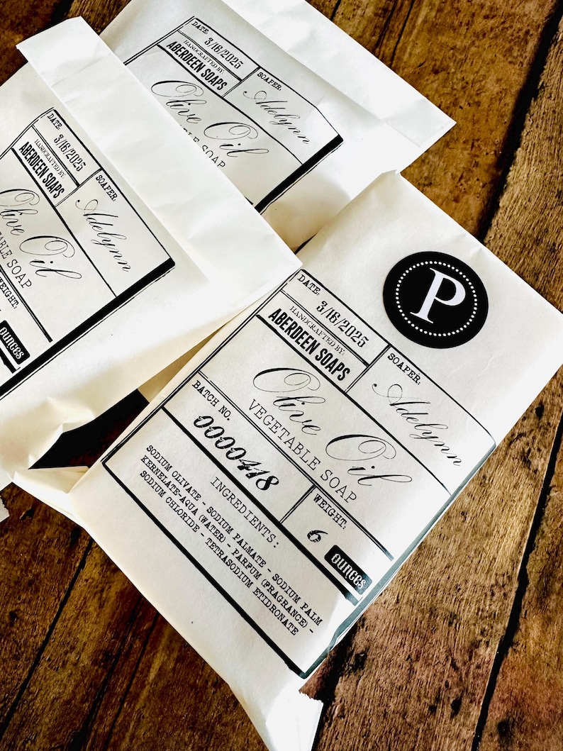 May include: Three white paper bags with black text and a black circle with a white letter P in the center. The text on the bags reads 'Date 3/16/2025', 'Handcrafted by Aberdeen Soaps', 'Olive Oil', 'Vegetable Soap', 'Batch No. 0000418', 'Weight 6 ounces', 'Ingredients: Sodium Olivate - Sodium Palmate - Sodium Palm Kernelate - Aqua (Water) - Parfum (Fragrance) - Sodium Chloride - Tetrasodum Etidronate', 'Soapfer Adelynn'.