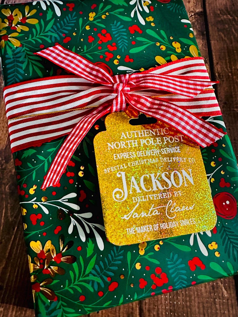 Puede incluir: Un regalo de Navidad envuelto en papel verde con un dise&ntilde;o floral, atado con una cinta a rayas rojas y blancas. Una etiqueta dorada con purpurina dice "AUTHENTIC NORTH POLE POST" y "JACKSON" con "DELIVERED BY Santa Claus."