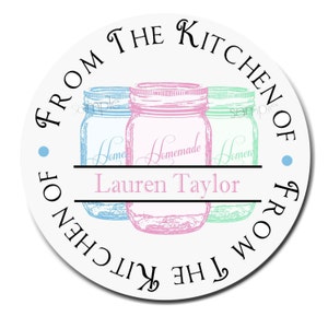 May include: Round white sticker with the text "From the Kitchen of" and "From the Kitchen of" in a circle around three mason jars. The jars are blue, pink, and green. The text "Homemade" is written on the pink jar. The text "Lauren Taylor" is written below the jars.