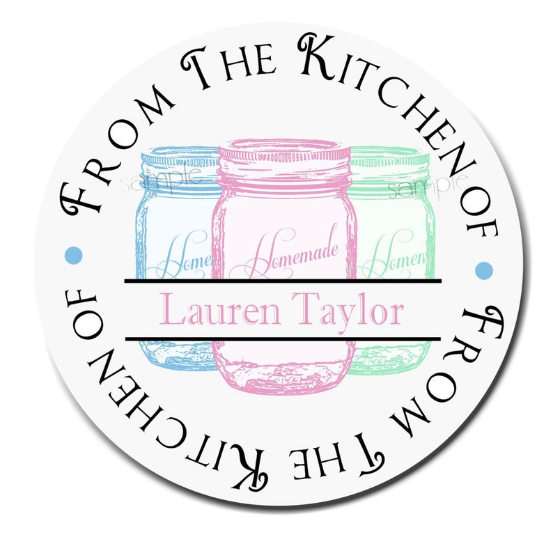 May include: Round white sticker with the text "From the Kitchen of" and "From the Kitchen of" in a circle around three mason jars. The jars are blue, pink, and green. The text "Homemade" is written on the pink jar. The text "Lauren Taylor" is written below the jars.