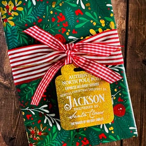 Puede incluir: Un regalo de Navidad envuelto en papel floral verde, atado con una cinta a rayas rojas y blancas y una etiqueta dorada. La etiqueta dice "Authentic North Pole Post Express Delivery Service" y "Jackson entregado por Santa Claus."