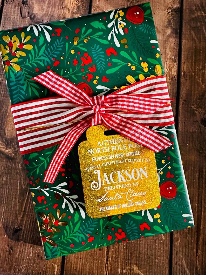 Puede incluir: Un regalo de Navidad envuelto en papel floral verde, atado con una cinta a rayas rojas y blancas y una etiqueta dorada. La etiqueta dice "Authentic North Pole Post Express Delivery Service" y "Jackson entregado por Santa Claus."