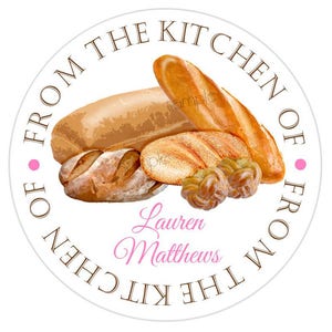 May include: Round white sticker with brown text that reads "From the Kitchen of" and "From the Kitchen of" in a circle. The sticker features a variety of breads, including a loaf of bread, a baguette, and a braided bread. The text "Lauren Matthews" is written in pink cursive.