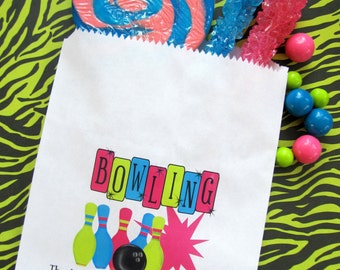 May include: White paper party favor bag with a bowling theme. The bag has a colorful graphic of bowling pins, a bowling ball, and a pink starburst. The text on the bag reads "Bowling" and "Thanks for making my birthday a strike! Olivia".