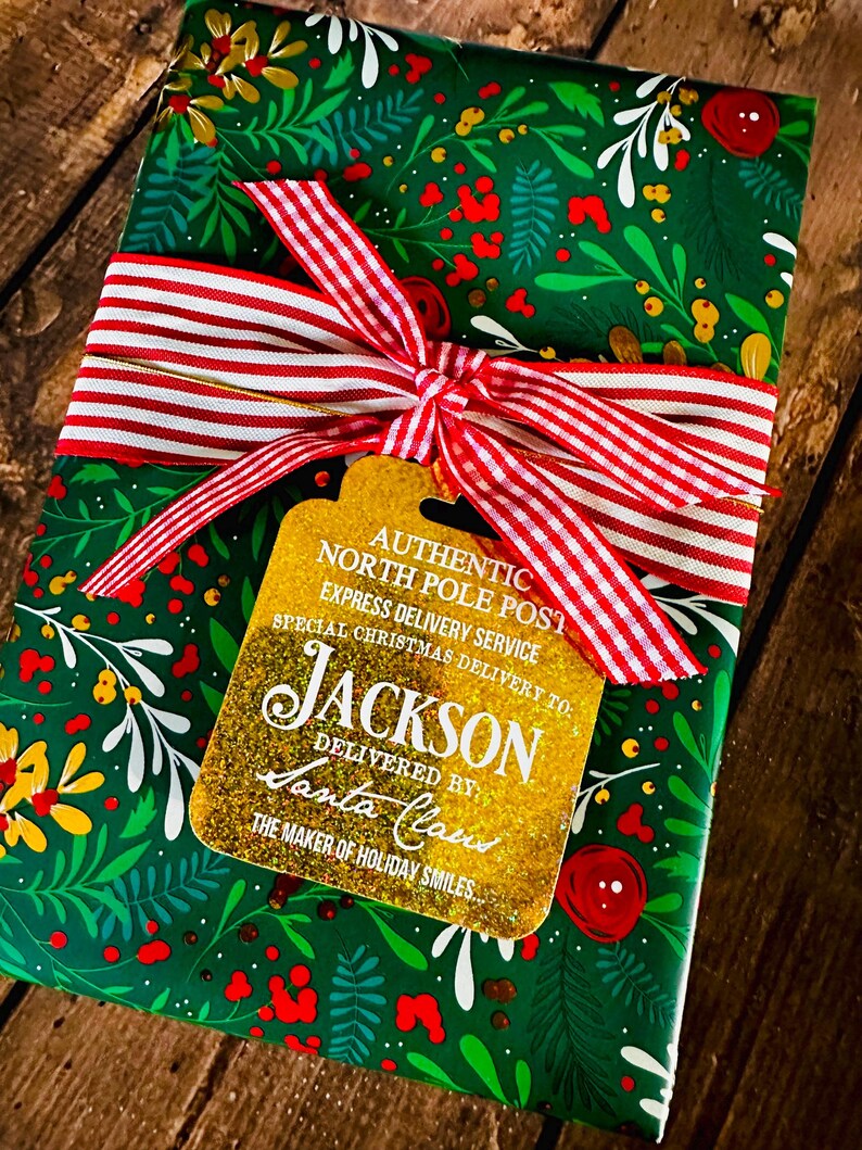 Puede incluir: Un regalo envuelto en papel verde con un dise&ntilde;o floral, atado con una cinta a rayas rojas y blancas. Una etiqueta dorada dice "AUTHENTIC NORTH POLE POST" y "JACKSON DELIVERED BY Santa Claus".