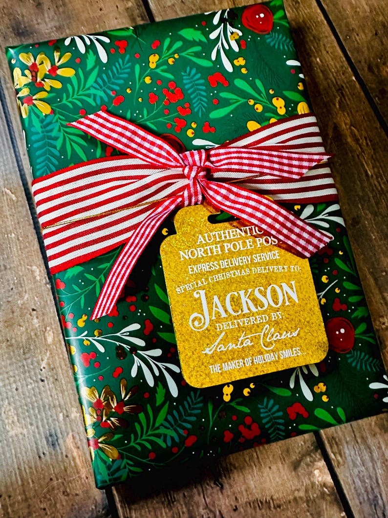 Puede incluir: Un regalo de Navidad envuelto en papel verde con un dise&ntilde;o floral. Una cinta a rayas rojas y blancas est&aacute; atada alrededor del regalo, con una etiqueta dorada que dice "AUTHENTIC NORTH POLE POST EXPRESS DELIVERY SERVICE SPECIAL CHRISTMAS DELIVERY TO JACKSON DELIVERED BY SANTA CLAUS THE MAKER OF HOLIDAY SMILES."