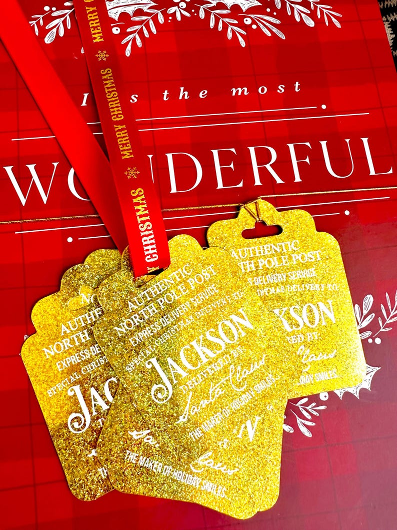 Puede incluir: Etiquetas de regalo doradas con purpurina con el texto "AUTHENTIC NORTH POLE POST" y "JACKSON" en blanco. Una cinta roja con "MERRY CHRISTMAS" est&aacute; drapeada sobre las etiquetas. El fondo es un patr&oacute;n de cuadros rojos y blancos.