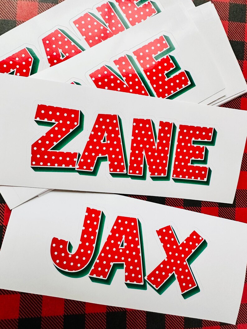 May include: A stack of white stickers with red and white polka dot letters spelling out the names "Zane" and "Jax". The letters have a green outline and a 3D effect.