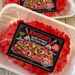 May include: Two packages of raw, red meat with a label that reads "Krueger's Slice and Dice Butcher Shop." The label features a gruesome display of eyeballs and fingers. The packages are in white foam trays, wrapped in clear plastic.
