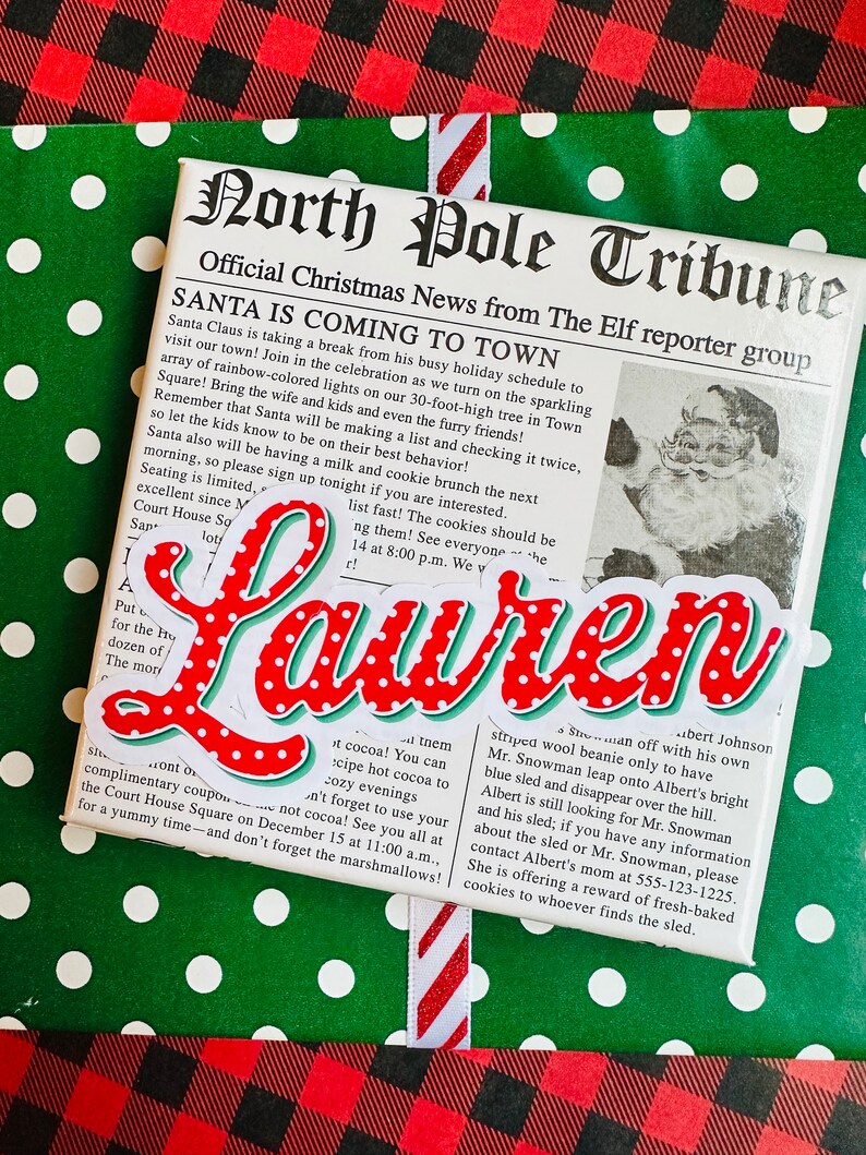 May include: A red and white Christmas-themed gift wrap with a newspaper clipping that reads "North Pole Tribune" and "Santa is Coming to Town". The newspaper clipping also includes a photo of Santa Claus. The gift wrap is decorated with white polka dots on a green background and red and black plaid.