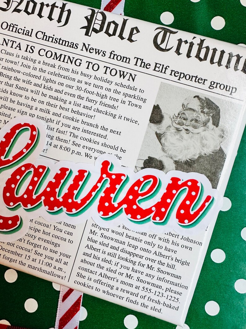 May include: A red and white Christmas-themed newspaper clipping with the headline "Santa is Coming to Town". The newspaper clipping is on a green background with white polka dots. The text on the clipping reads "Official Christmas News from The Elf reporter group".