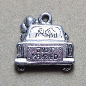 May include: A silver-colored charm in the shape of a car with the words "JUST MARRIED" on the license plate. The car has a couple inside and balloons on top, perfect for wedding-themed jewelry or crafts.