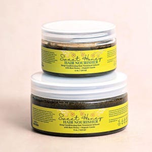 Può includere: Due barattoli rotondi in plastica di Sweet Honey Hair Nourisher impilati verticalmente. Le etichette gialle presentano testo nero, accenti floreali e indicano il contenuto come trattamento condizionante profondo con miele grezzo e cassia biologica, in 120 ml e 240 ml.