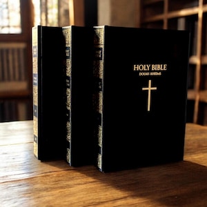 May include: Three black leather-bound books with gold lettering. The book on the right has the title "HOLY BIBLE DOUAY-RHEIMS" and a gold cross.