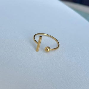 May include: A gold ring with a thin, vertical bar and a small sphere attached to the band.