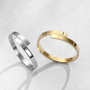 May include: Two simple, modern rings. One ring is silver and the other is gold. Both rings have a unique twist design.