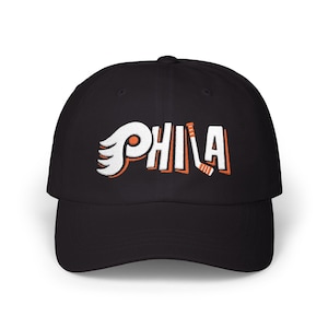 May include: Black baseball cap with the word "PHILA" embroidered in white and orange. The design incorporates a wing and hockey stick, representing a sports team.