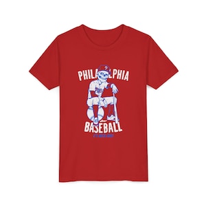 May include: Red t-shirt featuring a baseball-themed graphic. The design includes the text "PHILADELPHIA BASEBALL" and an illustration of a skeleton in a baseball uniform leaning on a bat.