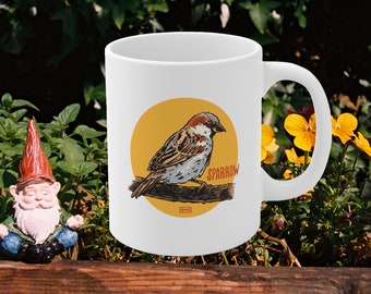 Puede incluir: Taza de cerámica blanca con una ilustración de un gorrión en un círculo amarillo. El gorrión es marrón, gris y blanco con el pecho rojo. El texto "SPARROW" está en letras rojas en el círculo.