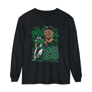 May include: Black long-sleeve t-shirt with a green and white graphic of a football player with the text "2023 Philadelphia Fly Eagles 26 Saquon".