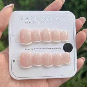 Op de afbeelding: Een set lichtroze persnagels met witte French tips, gepresenteerd in een witte verpakking. De verpakking is voorzien van de tekst "NAILSALON" en "Luxury Handmade Press on Nails".