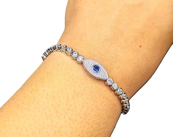 May include: Silver bracelet featuring a central oval charm with a blue center stone and surrounding white stones, resembling an eye. The bracelet is adorned with alternating round white stones. A delicate piece of jewelry.