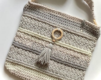 May include: A crocheted gray and white crossbody bag with a wooden ring and tassel. The bag has a long strap and is made with a textured stitch.
