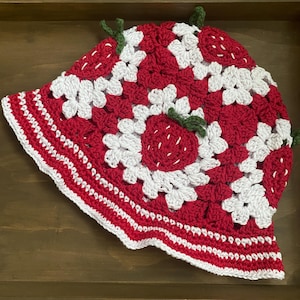 Può includere: Un cappello a secchiello all'uncinetto fatto a mano con un design a fragola. Il cappello è principalmente rosso con accenti bianchi e steli verdi. Il bordo è rifinito con punti all'uncinetto bianchi e rossi. Questo cappello è un accessorio unico.