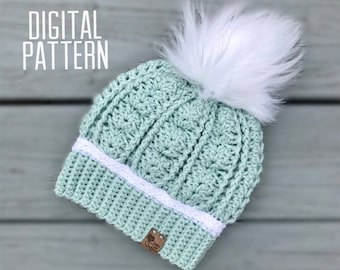 May include: A light green crochet beanie with a white pom pom and a white crocheted band. The beanie has a brown label with the text "Crochet Creations" on it. The text "DIGITAL PATTERN" is in the top left corner of the image. The text "JL CROCHET" is in the bottom right corner of the image.