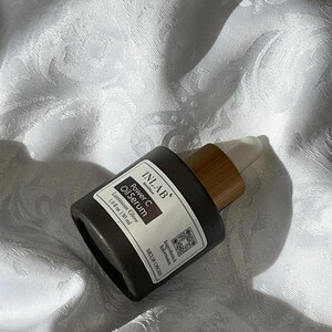 May include: A dark grey glass bottle with a bamboo dropper top. The bottle is labelled "INLAB" "Power C Oil Serum" "Luminous Glow" "1.0 fl oz (30 ml)" and "SKU# OSO".