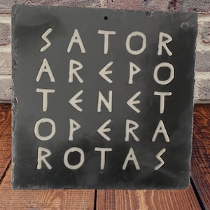 May include: A dark grey slate sign, square in shape, with the words "SATOR AREPO TENET OPERA ROTAS" etched in white. The sign has a hole for hanging and is set against a brick and wood backdrop.