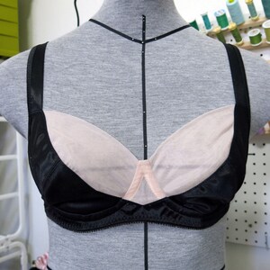 May include: A black bra with a nude mesh cup and black straps. The bra is on a dress form.