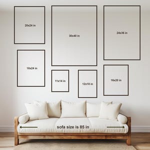 May include: A white sofa with a wooden frame and a measurement of 85 inches. The sofa is positioned in front of a white wall with several black picture frames of various sizes. The frames are labeled with measurements in inches.