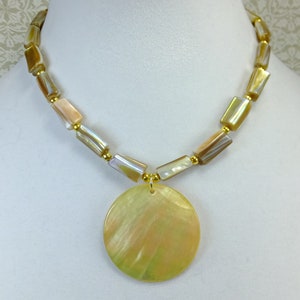 May include: A gold necklace with a large, round, iridescent shell pendant. The necklace is made of small, rectangular, iridescent shell beads.