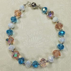 May include: A beaded bracelet with a magnetic clasp. The beads are iridescent and come in shades of blue, peach, and white.