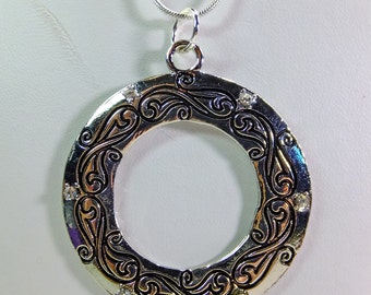 Large Metal Donut Pendant Enscribed with a Flowing Design and Tiny Crystal Embellishments on a Chain