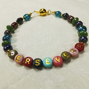 May include: A colorful beaded bracelet with gold letters spelling out the word "PERSEVERE". The bracelet has a magnetic clasp and is made with a variety of blue, green, red, pink, and brown beads.