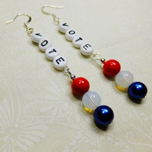 May include: A pair of silver earrings with white beads spelling "VOTE" and red, white, and blue beads.