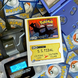 May include: A blue Game Boy Advance SP with a screen displaying a Pokemon Eon Ticket for the S.S. Tidal, which takes players from Lilycove City to Southern Island. The ticket is for Pokemon Ruby and Sapphire versions. The Game Boy is on top of a pile of Pokemon trading cards.