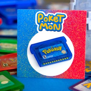 May include: A graphic with the words "Poket Mon" and a blue Pokemon game cartridge. The cartridge is centered on a white circle, set against a blue and red background. Other game cartridges are visible.