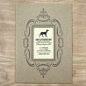 Peut inclure: Un tapis en papier brun avec un cadre d&eacute;coratif noir et une illustration en noir et blanc d'un chien. Le texte "Fancy Letterpress Mat" est imprim&eacute; sur le tapis, ainsi que des instructions pour l'utiliser et le site Web "pioneer-house.com".