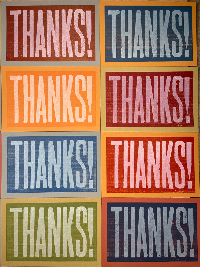 Puede incluir: Un conjunto de seis tarjetas con la palabra "THANKS!" impresa en blanco en cada tarjeta. Las tarjetas est&aacute;n dispuestas en dos filas de tres, con cada fila con un fondo de color diferente: marr&oacute;n, naranja, azul, rojo, azul y verde.