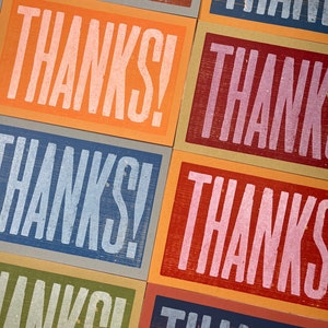 Puede incluir: Primer plano de una pila de tarjetas coloridas con la palabra "&iexcl;GRACIAS!" impresa en cada tarjeta. Las tarjetas est&aacute;n hechas de diferentes materiales y tienen un aspecto texturizado.