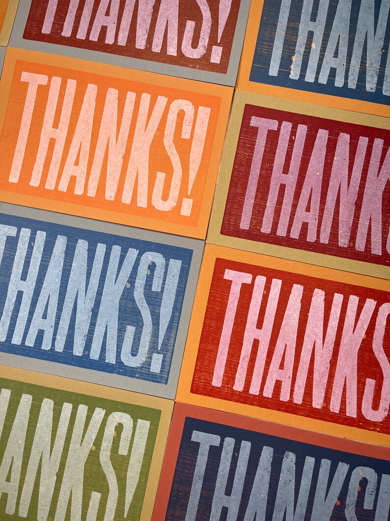 Puede incluir: Primer plano de una pila de tarjetas coloridas con la palabra "&iexcl;GRACIAS!" impresa en cada tarjeta. Las tarjetas est&aacute;n hechas de diferentes materiales y tienen un aspecto texturizado.