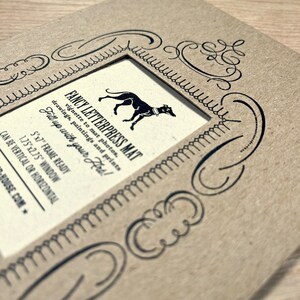 Peut inclure: Un tapis en papier brun avec une bordure d&eacute;corative et une d&eacute;coupe pour une photo de 12,7x17,8 cm. Le tapis porte l'inscription "FANCY LETTERPRESS MAT" et "Fill up with your Hrt!" imprim&eacute;e dessus.