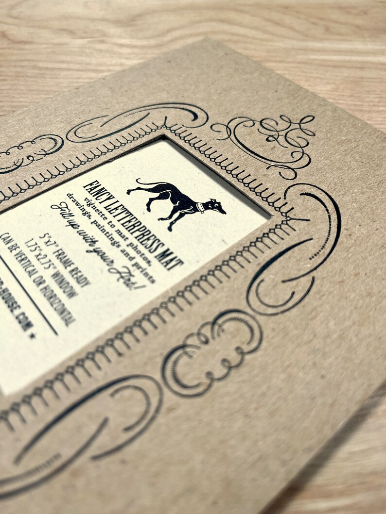 Peut inclure: Un tapis en papier brun avec une bordure d&eacute;corative et une d&eacute;coupe pour une photo de 12,7x17,8 cm. Le tapis porte l'inscription "FANCY LETTERPRESS MAT" et "Fill up with your Hrt!" imprim&eacute;e dessus.