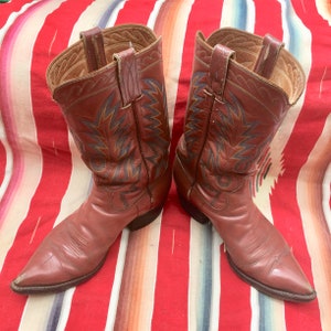 May include: A pair of brown leather cowboy boots with intricate stitching and pointed toes. The boots have a decorative pattern on the shaft.