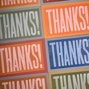 Puede incluir: Seis tarjetas con la palabra "THANKS!" impresa en letras blancas. Cada tarjeta tiene un fondo de color diferente: rosa, verde, naranja, azul, marr&oacute;n y verde claro.