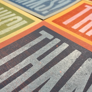 Puede incluir: Primer plano de un conjunto de tarjetas con diferentes colores y texturas. Cada tarjeta presenta una palabra en negrita, en blanco. Las palabras son "THANKS", "YOU'RE", "AMAZING", "I LOVE" y "THAT".